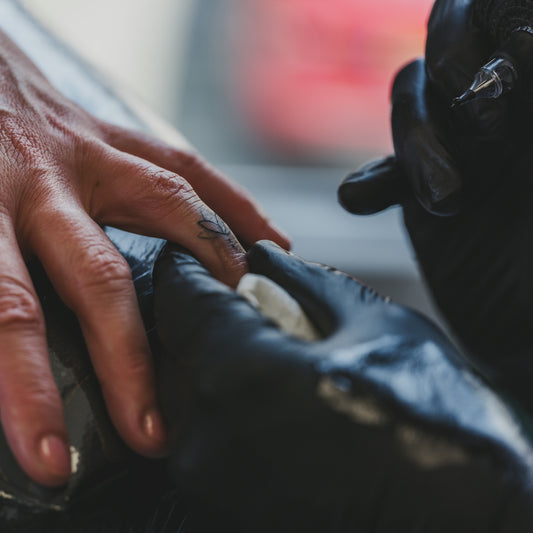 Artist tattooing a small design on a finger.