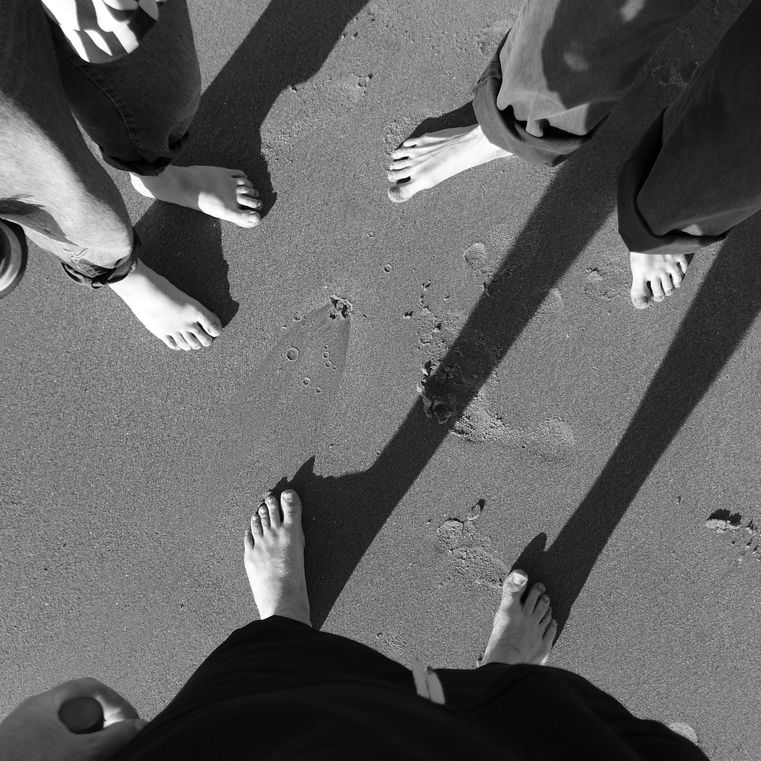 Bare feet and long shadows on sandy ground.