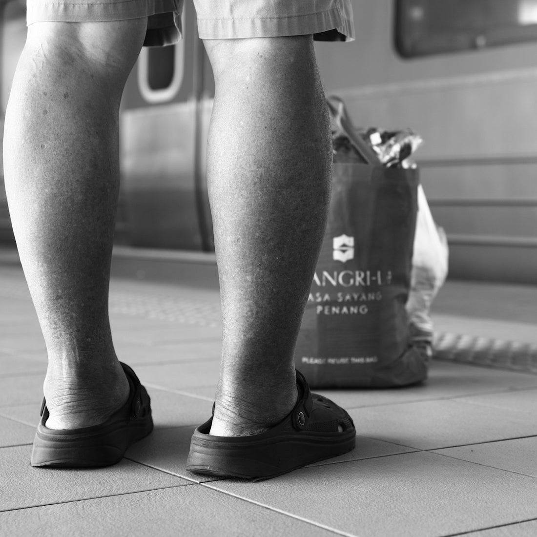 Man's legs in clogs standing beside a shangri-la bag.